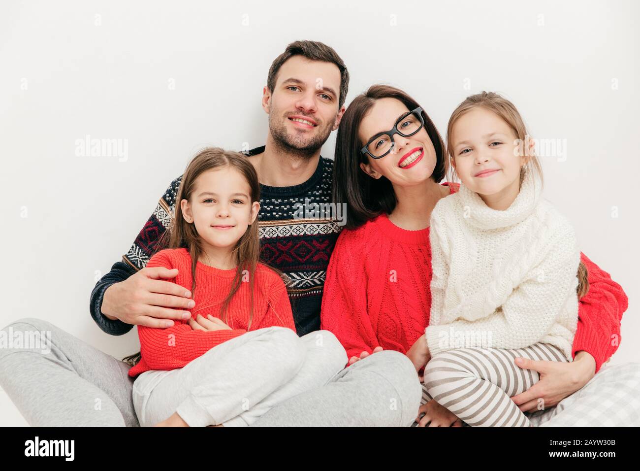 Family Portrait: Mutter, Vater und zwei Schwestern schauen direkt in die Kamera, haben positive Ausdrücke, und Lächeln freudig umarmt, isoliert Stockfoto