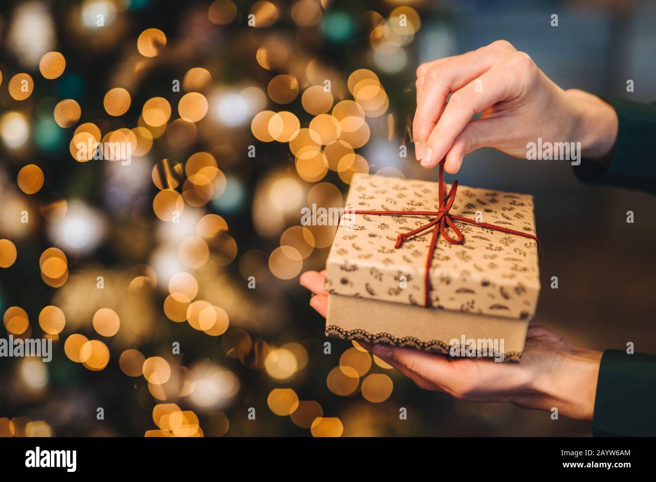 Nicht erkennbare Frau wrappes Geschenkbox über Weihnachten Baum mit leuchtenden Lichter und Kränze. Dekoriert präsentieren, in Frau ein Hände. Urlaub und celeb Stockfoto