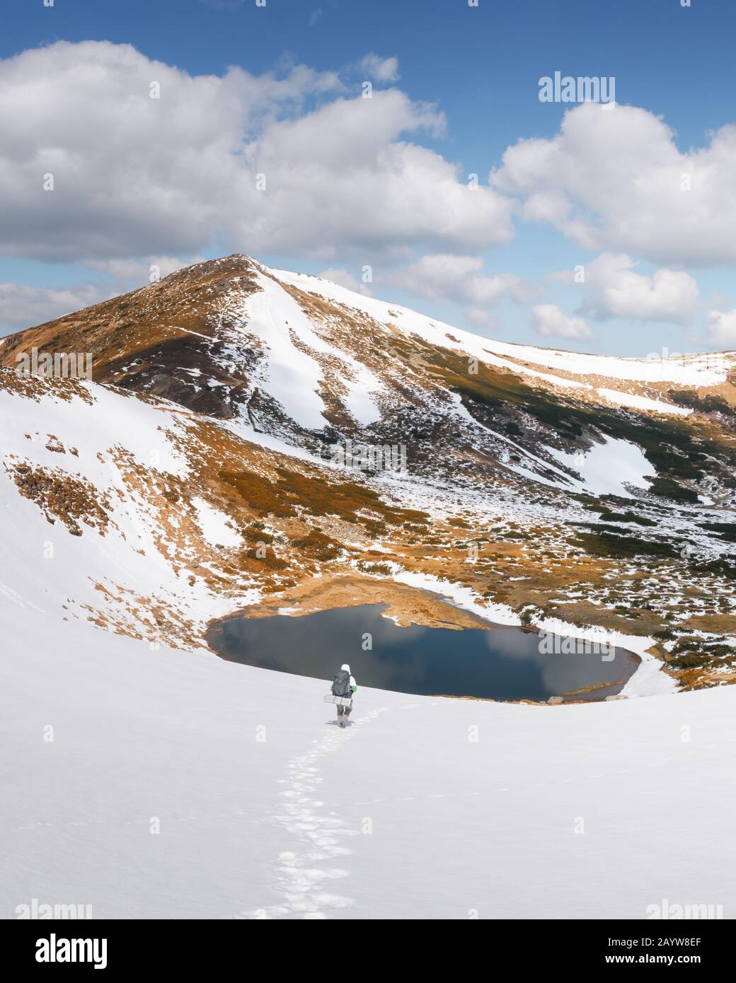Herrliche Landschaft mit See in den schneereichen Bergen im Frühling. Wanderer mit Rucksack im Schnee Stockfoto