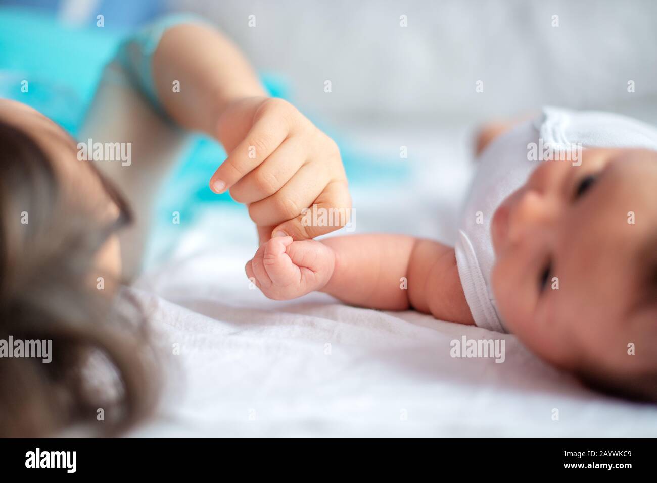 Neugeborenes Baby mit ihrer älteren Schwester zusammen auf dem Bett halten einander die Hand Stockfoto