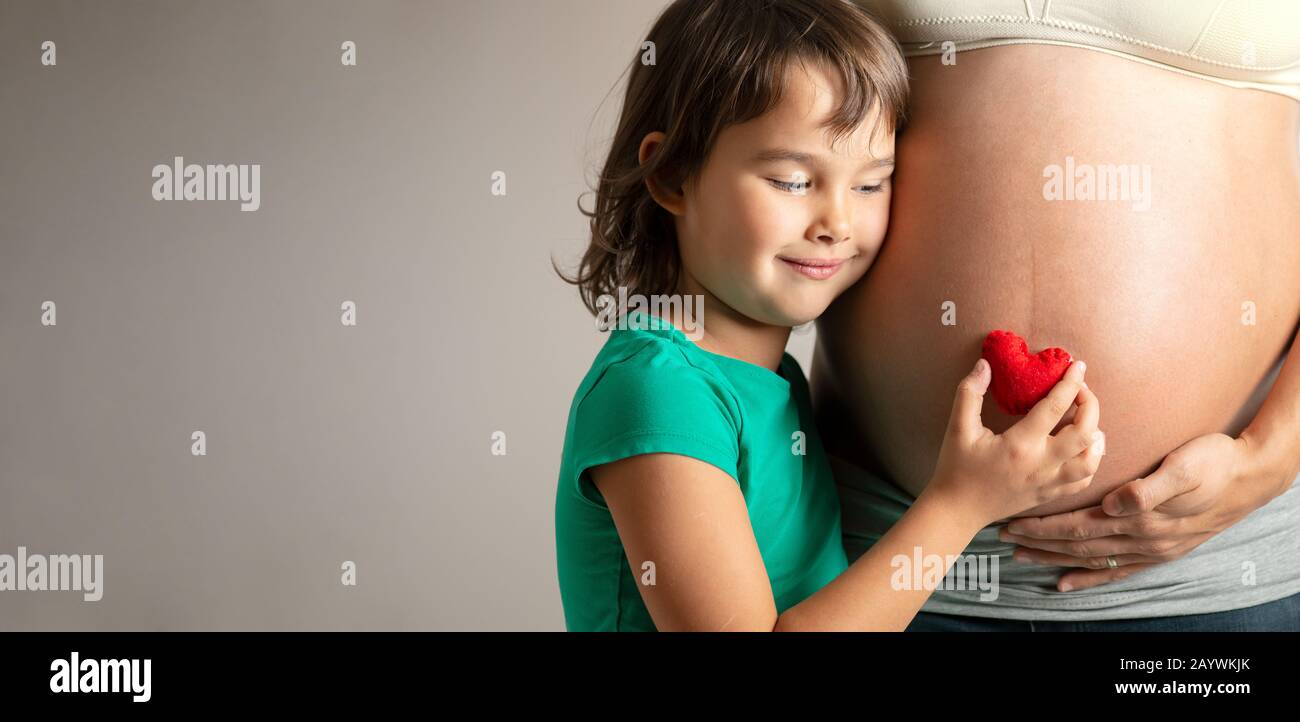 Zugeschnittenes Bild eines schönen Mädchens mit rotem Herz in der Hand über den Bauch ihrer Mutter Stockfoto