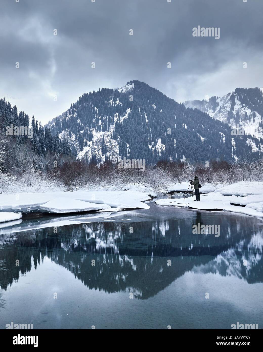 Landschaftsfotograf mit Kamera auf Stativ in epischer Landschaft ow Wintersee in den Bergen mit Reflexion. Stockfoto
