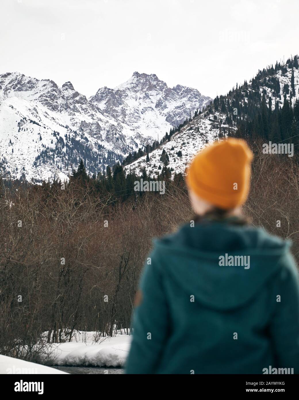 Das Frauenporträt in gelbem Hut ist gegen das epische Snowy-Gebirge in Kasachstan unscharf Stockfoto