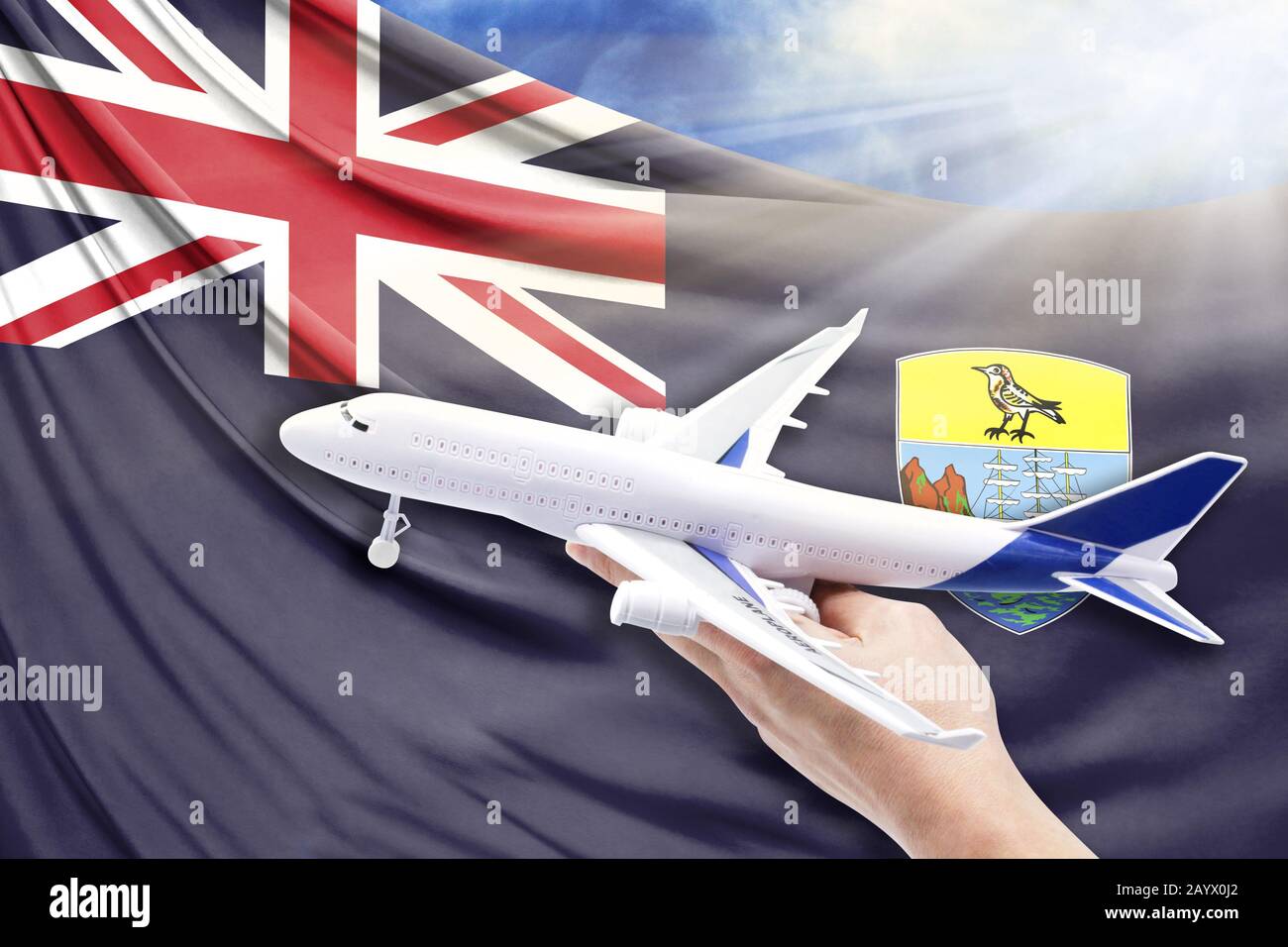 Flugzeug in der Hand mit Nationalflaggen von St. Helena auf blauem Himmel mit Sonnenstrahlen Stockfoto