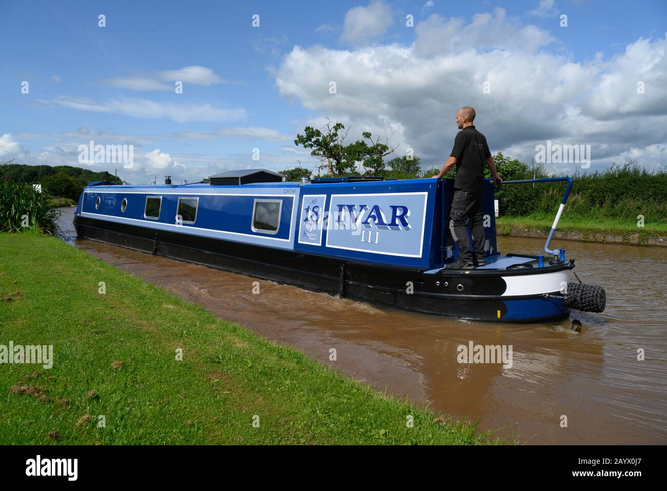 Narrowboat nannte Ivar III, der den Shropshire Union Canal in Cheshire bei strahlendem Sonnenschein und unter blauem Himmel mit einem Mann an der Deichsel passiert. Stockfoto