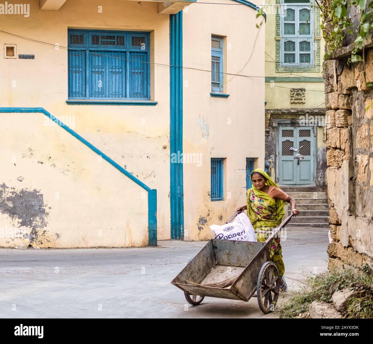 Eine Indianerin in einem grünen Sari schiebt einen leeren Wagen durch die ruhigen Straßen in einem Wohngebiet der Stadt Diu. Stockfoto