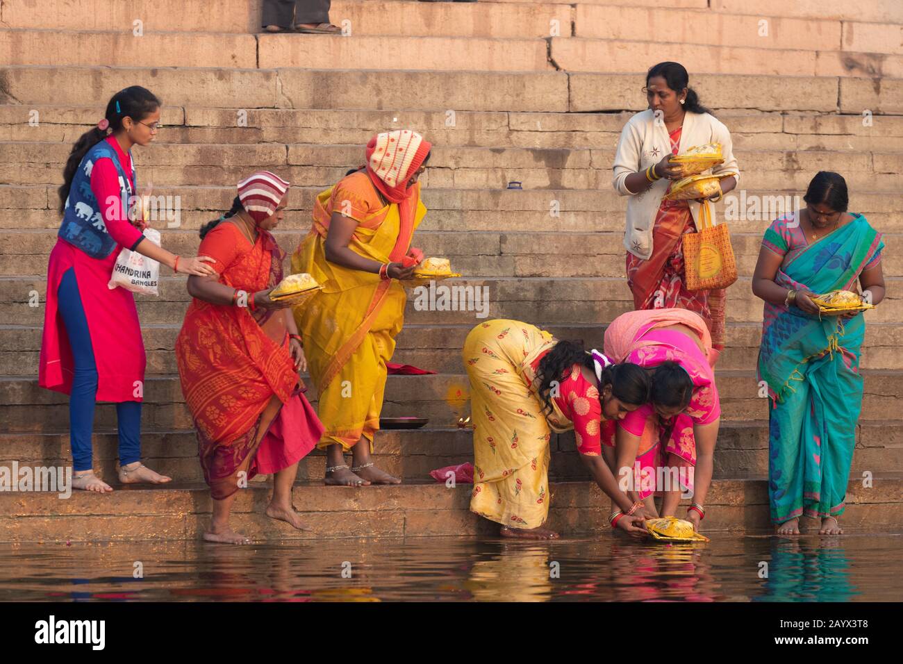 Varanasi, INDIEN, 18. JANUAR 2019: EINE Gruppe von Frauen, die bunte traditionelle Kleider tragen, betet, bevor sie bei Sonnenaufgang ein spirituelles Bad beginnen Stockfoto