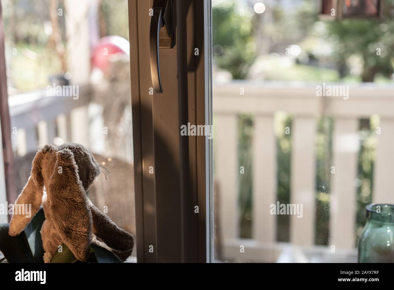 Der Osterhase blickt erwartungsvoll aus dem Fenster über die Veranda in den Garten. Hochwinkelige Ansicht, Nahaufnahme. Stockfoto