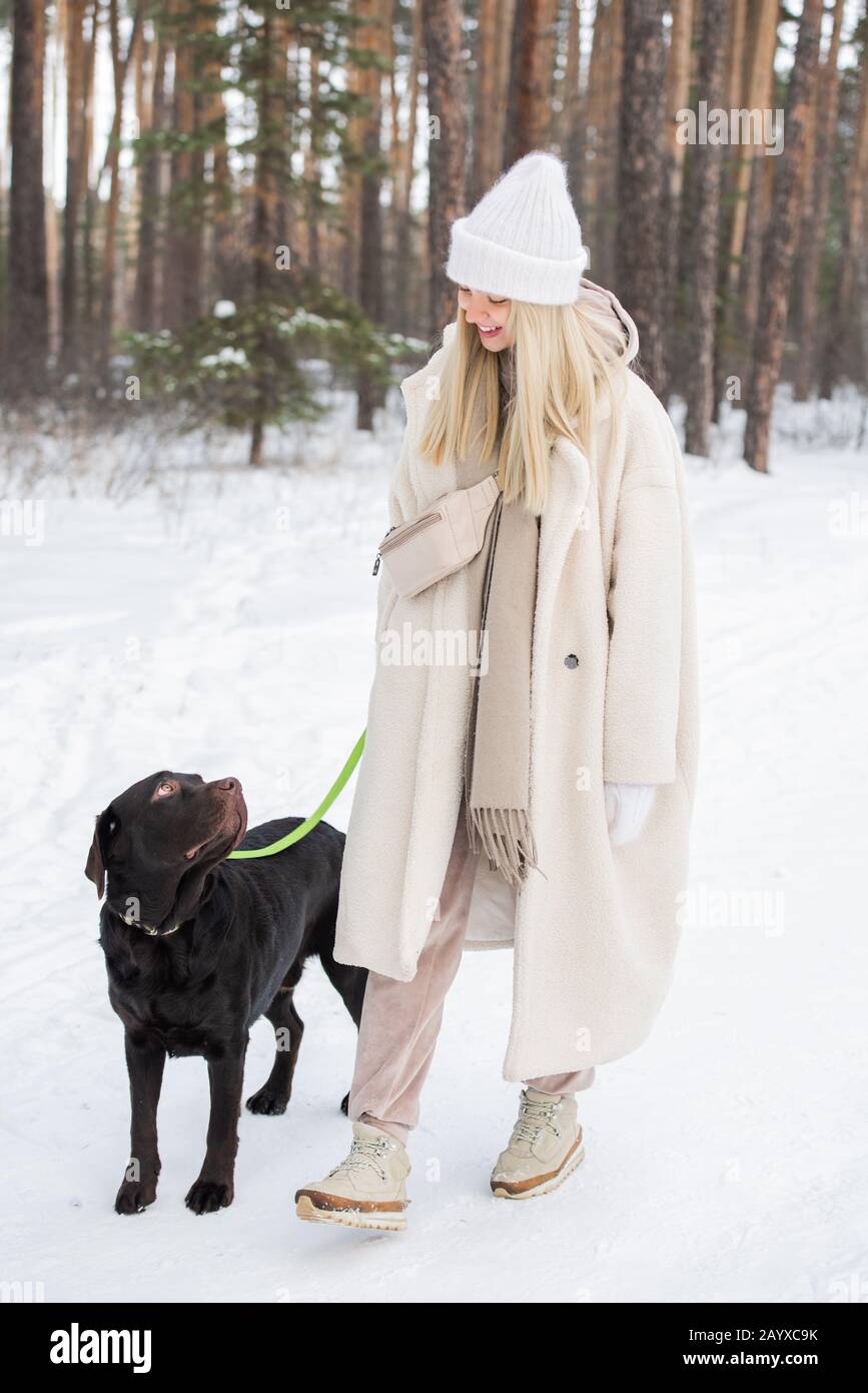 Horizontaler Schuss von jungen Frauen mit Kunstfellmantel, die mit ihrem schönen Hund am Wintertag im Freien verbringen Stockfoto