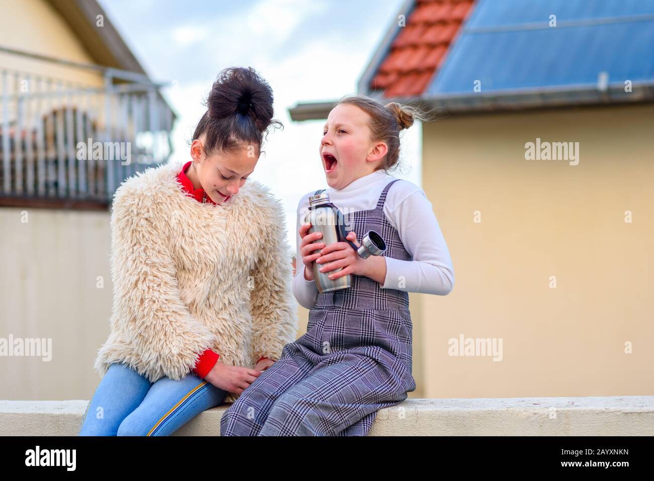 Porträt zwei Teenager mit Zittern und Gefühl kalt, mit Zähnen aus Kälte auf dem Dach der Stadt. Junges Mädchen, das wiederverwendbare Flasche mit heißem Tee hält und wegen des starken Windes und der Kälte schreit. Stockfoto