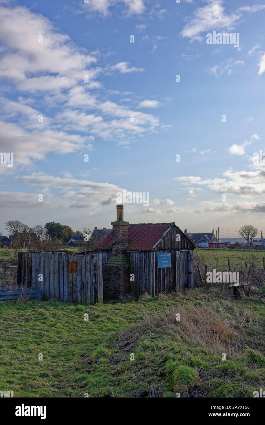 Eine verlassene und verderbliche Eisenbahnhütte mit blauem Abfahrschild neben der Hauptstrecke der East Coast Rail zwischen Edinburgh und Aberdeen. Stockfoto