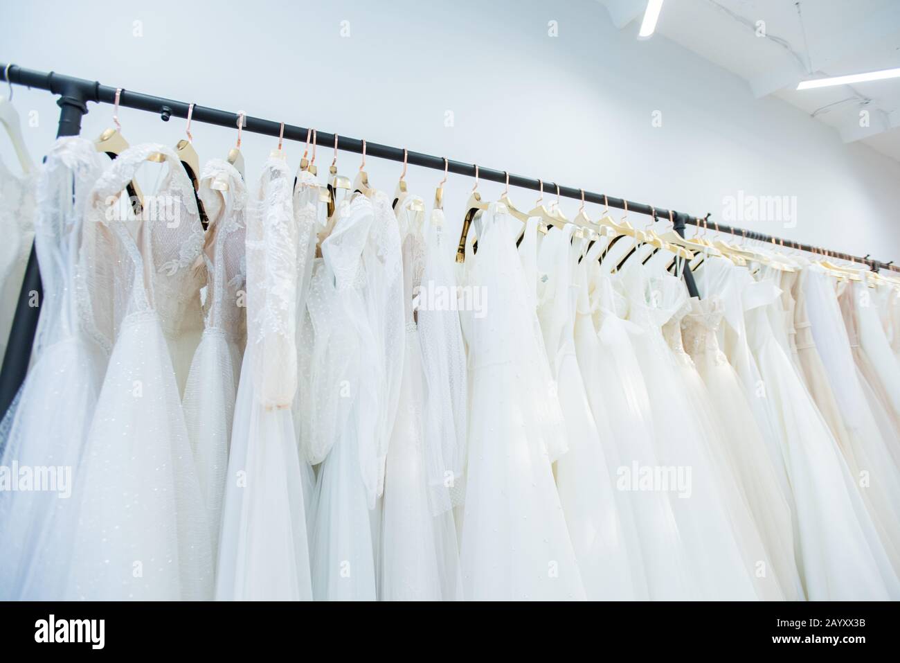 Horizontaler Tiefwinkel keine Personen, die im modernen brautkleidungsstudio auf Kleiderschienen von Hochzeitsgeigwaren erschossen wurden Stockfoto