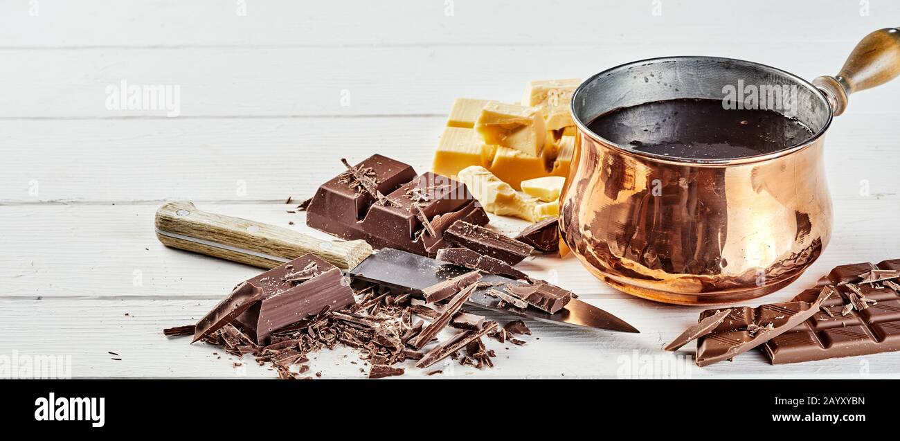 Bereiten Sie eine Schokoladensauce zu, oder tauchen Sie mit gehackten und durchblätterten verschiedenen Stäben neben einem Kupfertopf mit geschmolzener Schokolade in einem Bannerformat über weißem wo Stockfoto