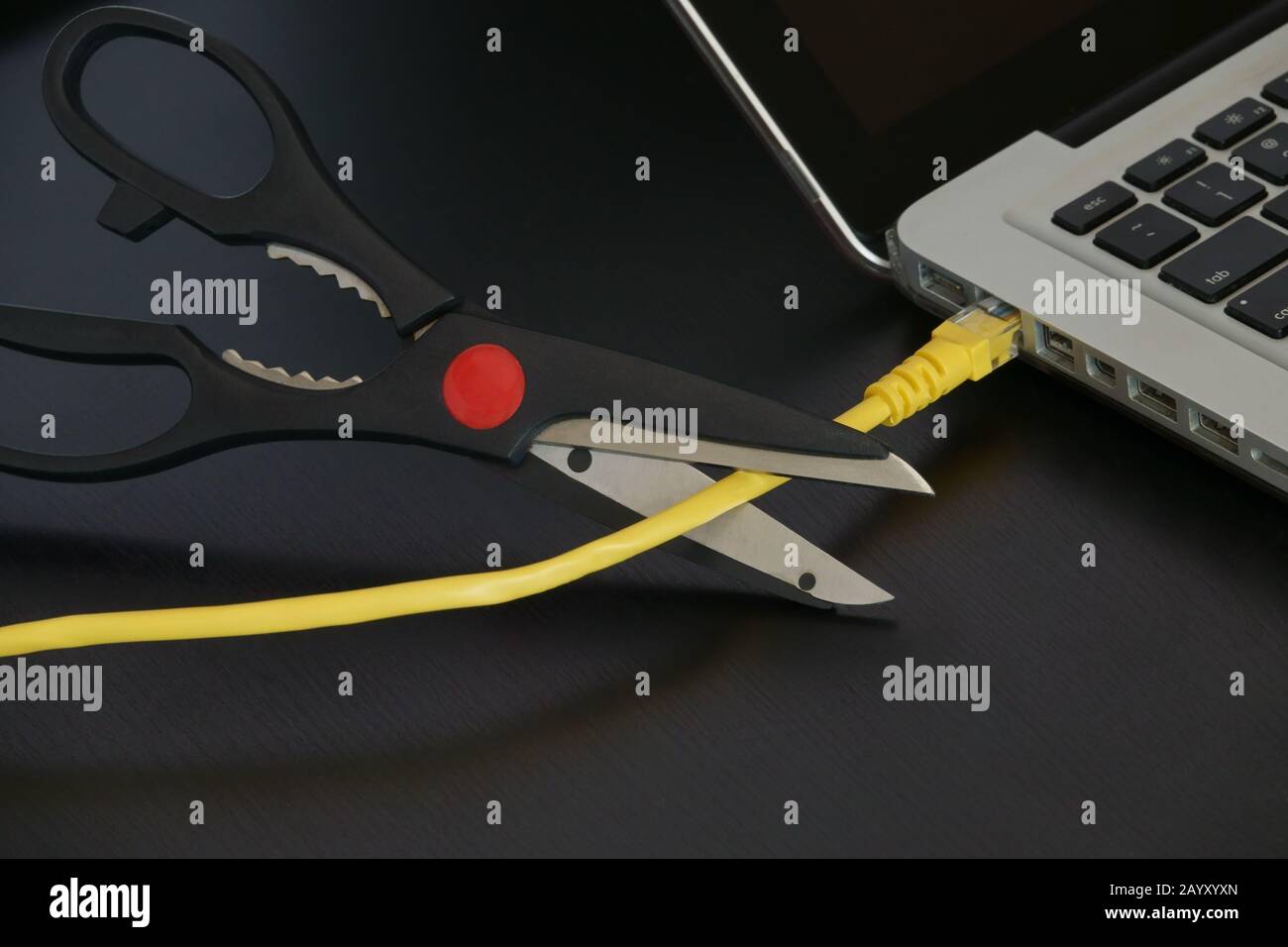 Eine scharfe Schere wird kurz vor dem Schneiden eines gelben ethernet-internetkabels angezeigt, das an einen Laptop-Computer angeschlossen ist. Stockfoto