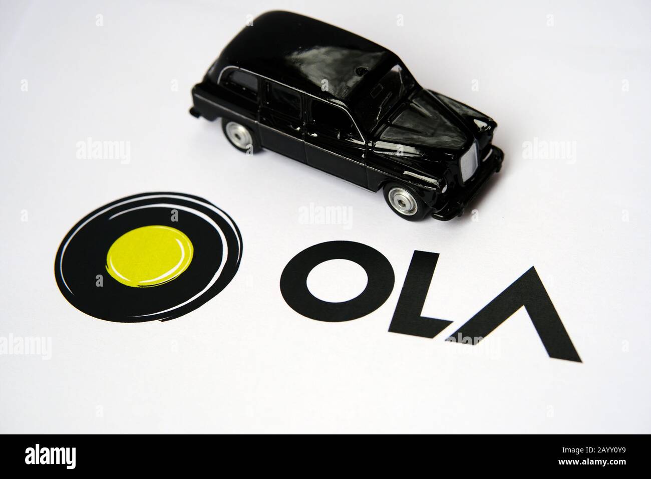 OLA-App-Logo auf Papierbroschüre und schwarze Kabine auf dem verschwommenen Hintergrund. OLA-Kabinen sind ein Unternehmen für die Mitfahrgelegenheit. Selektiver Fokus. Stockfoto