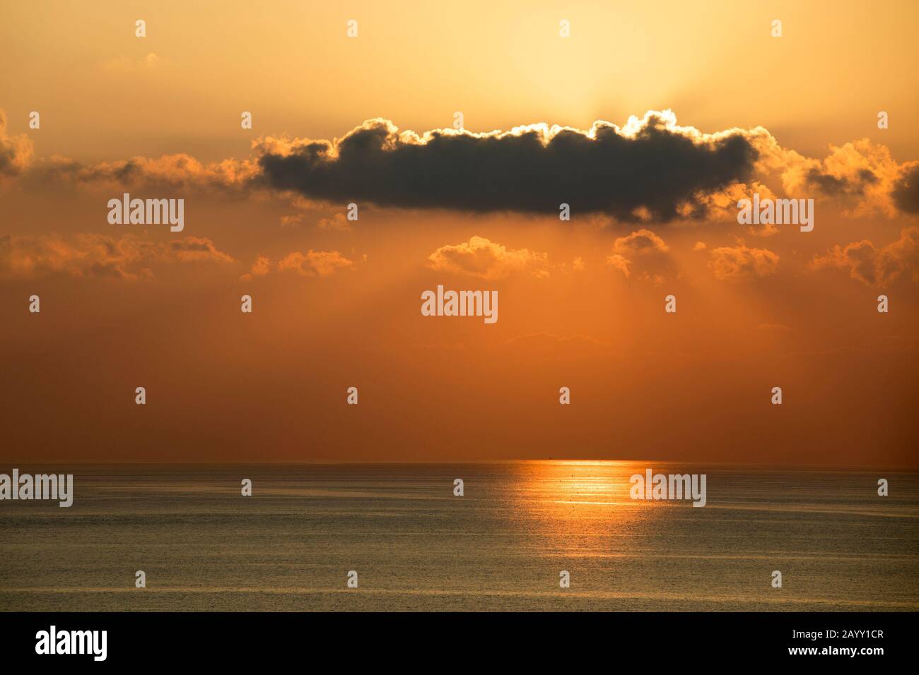 Dunkle Wolken blockieren die untergehende Sonne am orangefarbenen Abendhimmel über dem Mittelmeer Stockfoto
