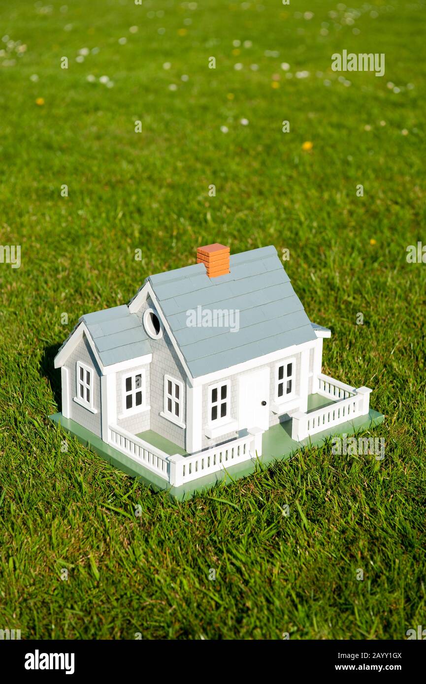 Miniaturhaus mit weißem Pickelzaun, das mitten auf einem grünen Rasenplatz steht Stockfoto