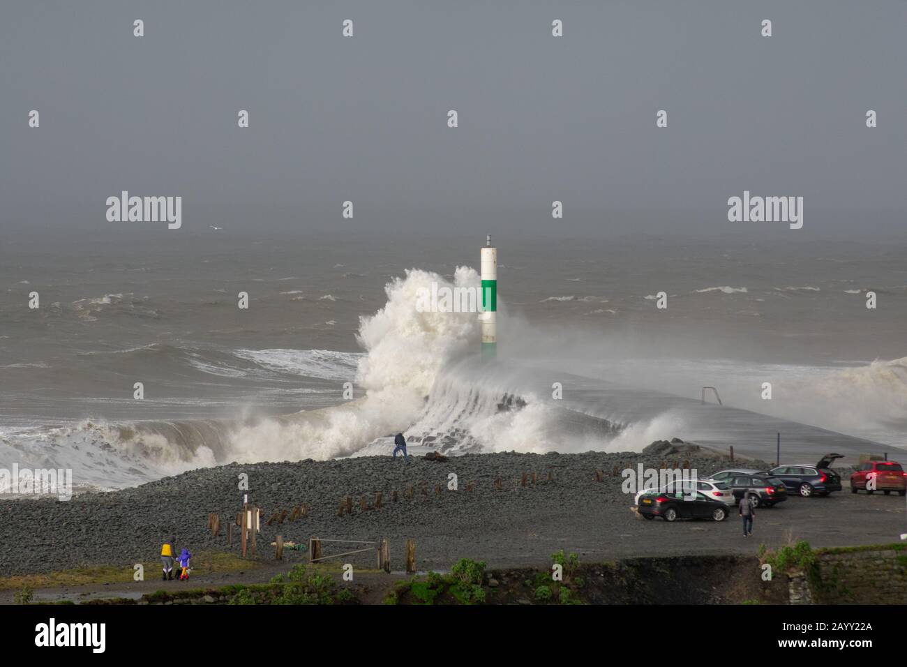 Stürmisches Wetter erzeugt große Wellen, die in Aberystwyth, Wales schwelgen, während Zuschauer von der Größe der Wellen in den Schatten gestellt werden. Stockfoto