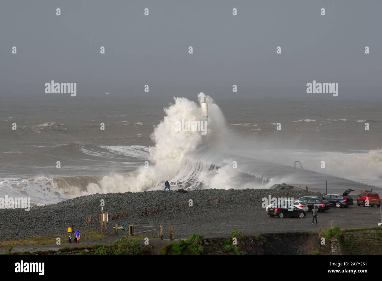 Stürmisches Wetter erzeugt große Wellen, die in Aberystwyth, Wales schwelgen, während Zuschauer von der Größe der Wellen in den Schatten gestellt werden. Stockfoto