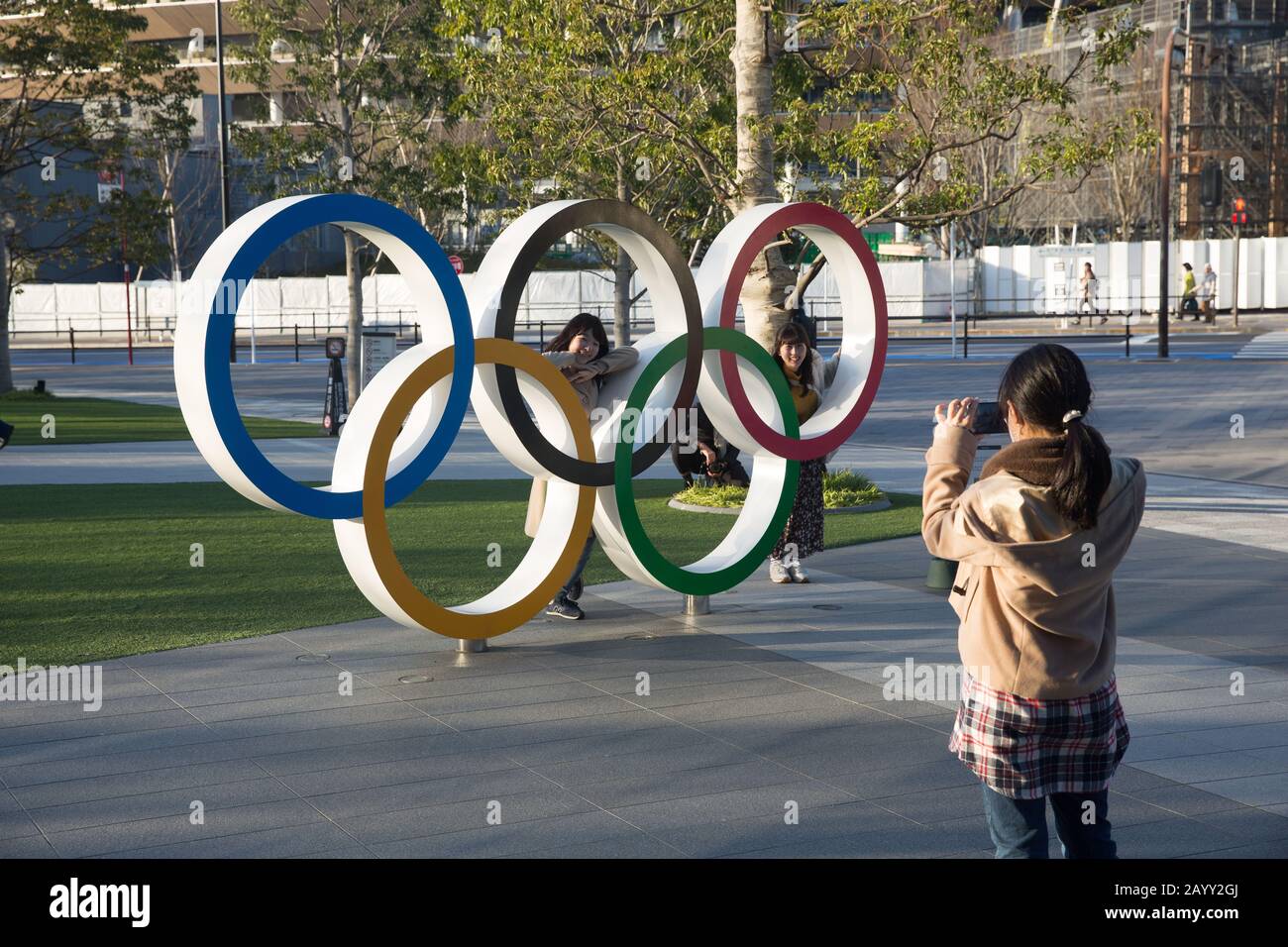 Fotos von Frauen, die hinter den Olympischen Ringen in der Nähe des Olympischen Museums in Japan und des neuen Nationalstadions in Tokio aufgenommen wurden. Das Stadion wird als Hauptstadion für die Eröffnungs- und Abschlussfeier sowie für die Leichtathletik-Veranstaltungen bei den Olympischen Sommerspielen in Tokio 2020 und Paralympischen Olympischen Sommerspielen dienen Spiele. Stockfoto