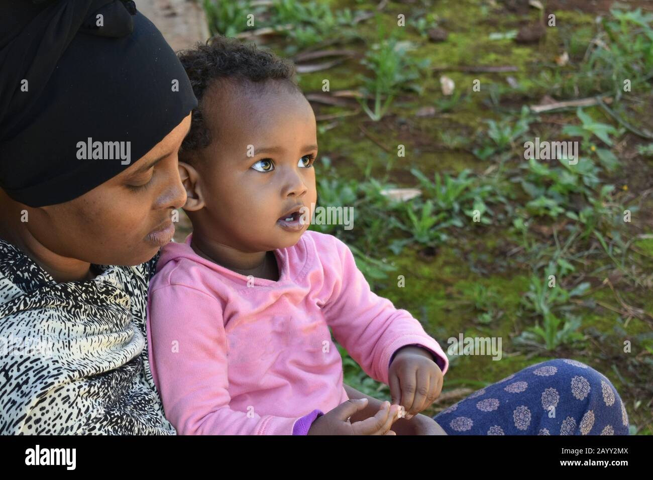 Ein süßes kenianisches Baby sitzt auf dem Schoß ihrer Mutter im Freien. Konzept der Zweisamkeit Stockfoto