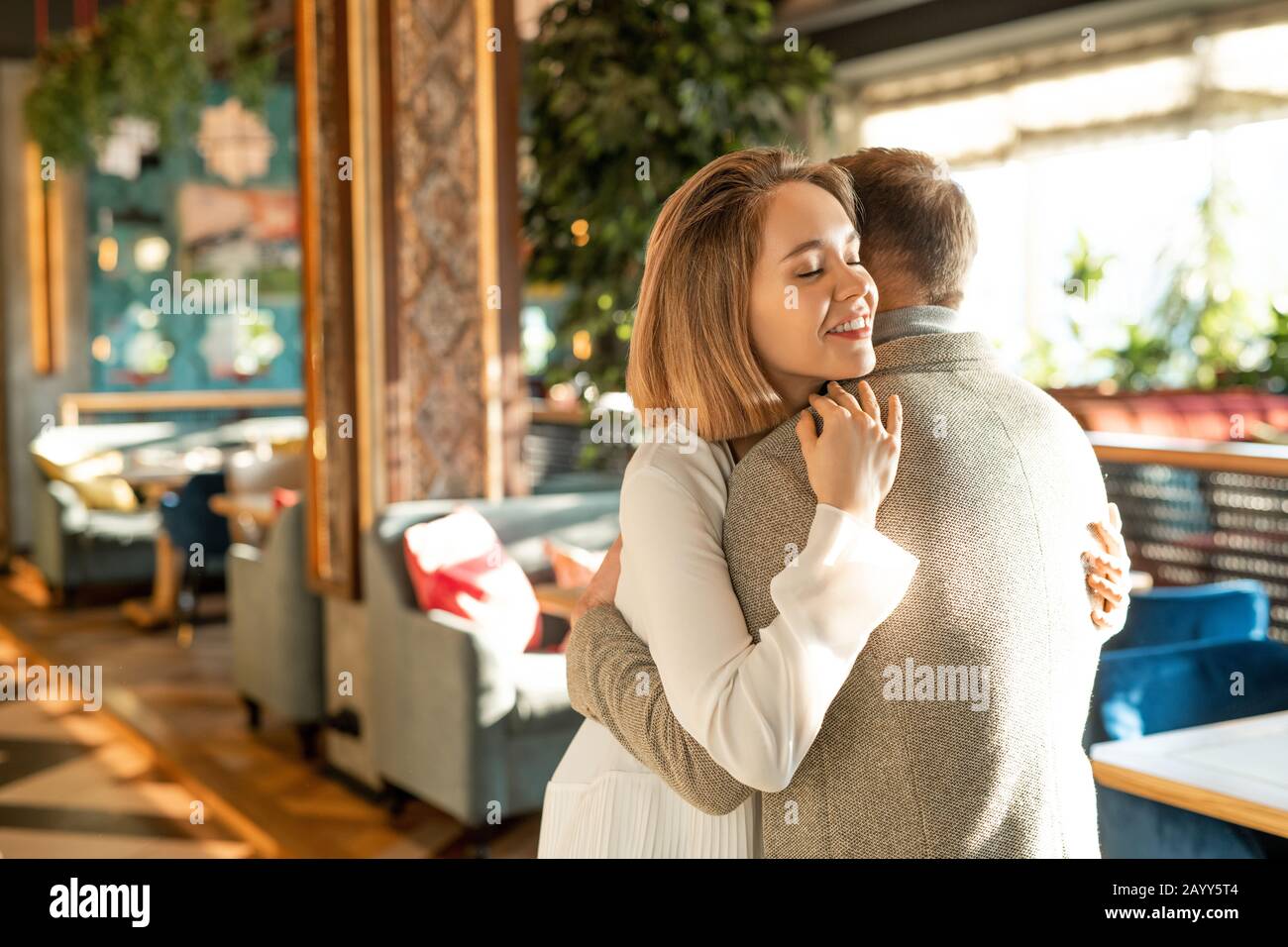 Fröhlicher junger Mann und Frau in Liebe begrüßen sich mit Umarmung im modernen Restaurant, horizontaler Mittelschuss Stockfoto