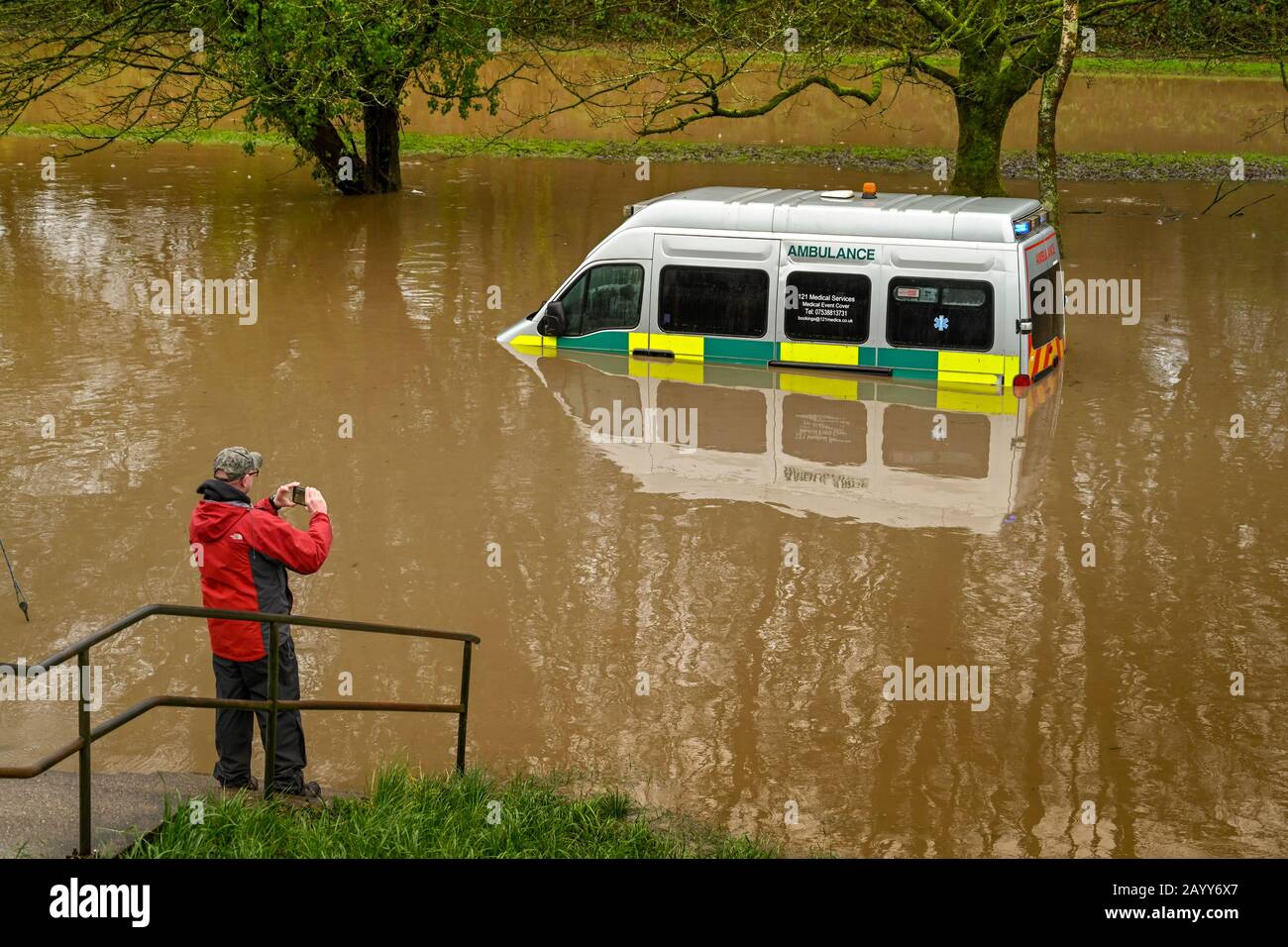 NANTGARW, IN DER NÄHE VON CARDIFF, WALES - FEBRUAR 2020: Person, die ein Bild von einem Krankenwagen machte, der im Sturmwasser untertaucht war, nachdem der Fluss Taff seine Ufer platzte Stockfoto