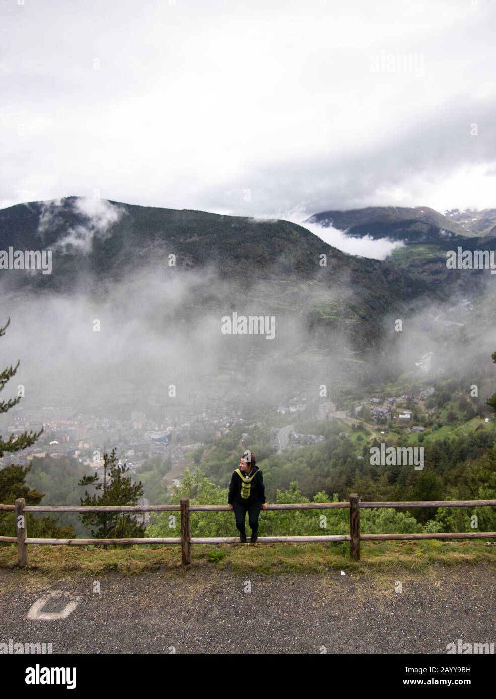 Touristenmädchen sitzt auf einem Holzzaun, während der Bergwanderung, mit Pyrenäenbergen im Hintergrund. Ein kleines Dorf von Encamp, in Andorra gelegen Stockfoto