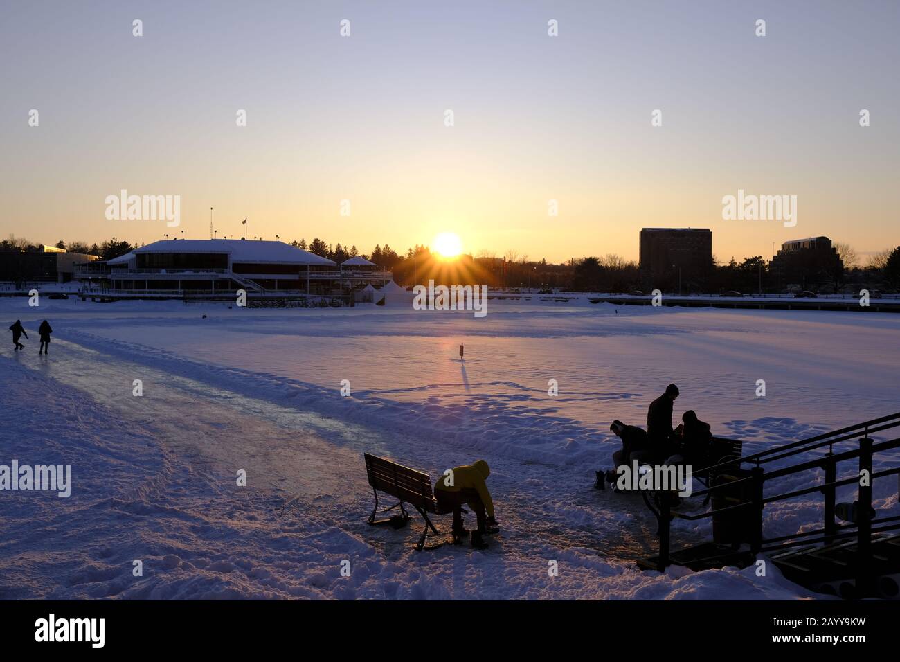 Skater legen an/nehmen Stiefel an der Kippewa-Einfahrt zum Rideau-Kanal-Sketeway ab, während die Sonne an einem kalten Wintertag untergeht. Stockfoto