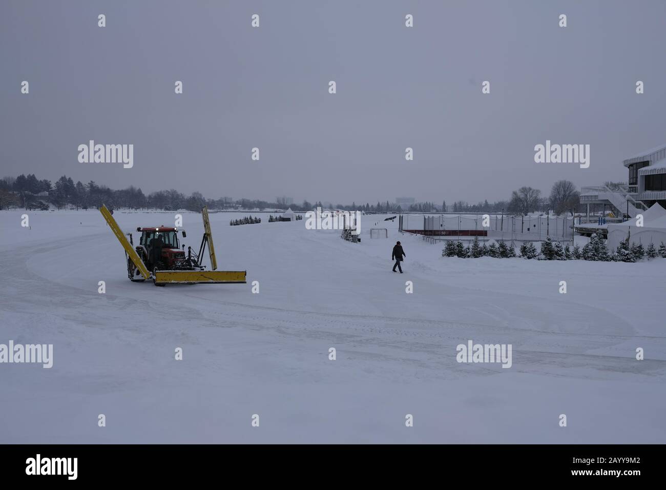 Ein Traktor, der sich als Schneepflug verdoppeln wird, löscht die Oberfläche des Rideau-Kanals als Pendler über das Eis. Ottawa, Ontario, Kanada. Stockfoto