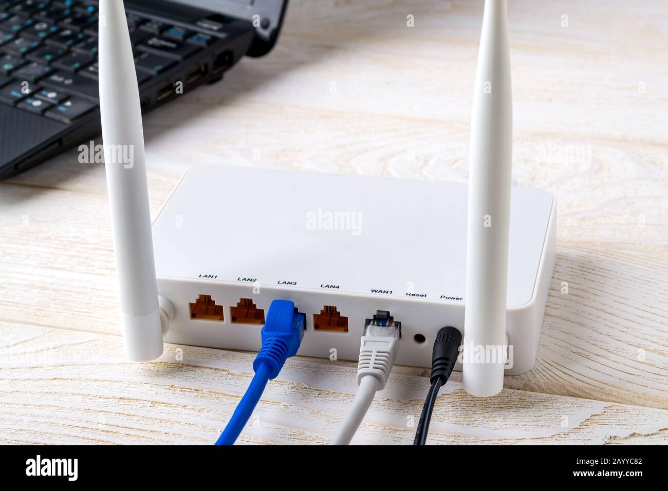 Netzwerkkabel, die mit einem weißen WLAN-Router in der Nähe eines Laptops  auf einem weißen Holztisch verbunden sind. WLAN-Router mit auf einem Tisch  eingesteckten Internetkabeln Stockfotografie - Alamy