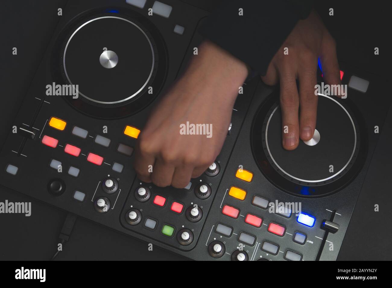 DJ spielt Musik ab. Sound Mixer Controller mit Knöpfen und Schiebereglern nah oben. Hände auf dem Mischdeck und Drehtische bei Dunkelheit mit beleuchteten Bedienelementen Stockfoto