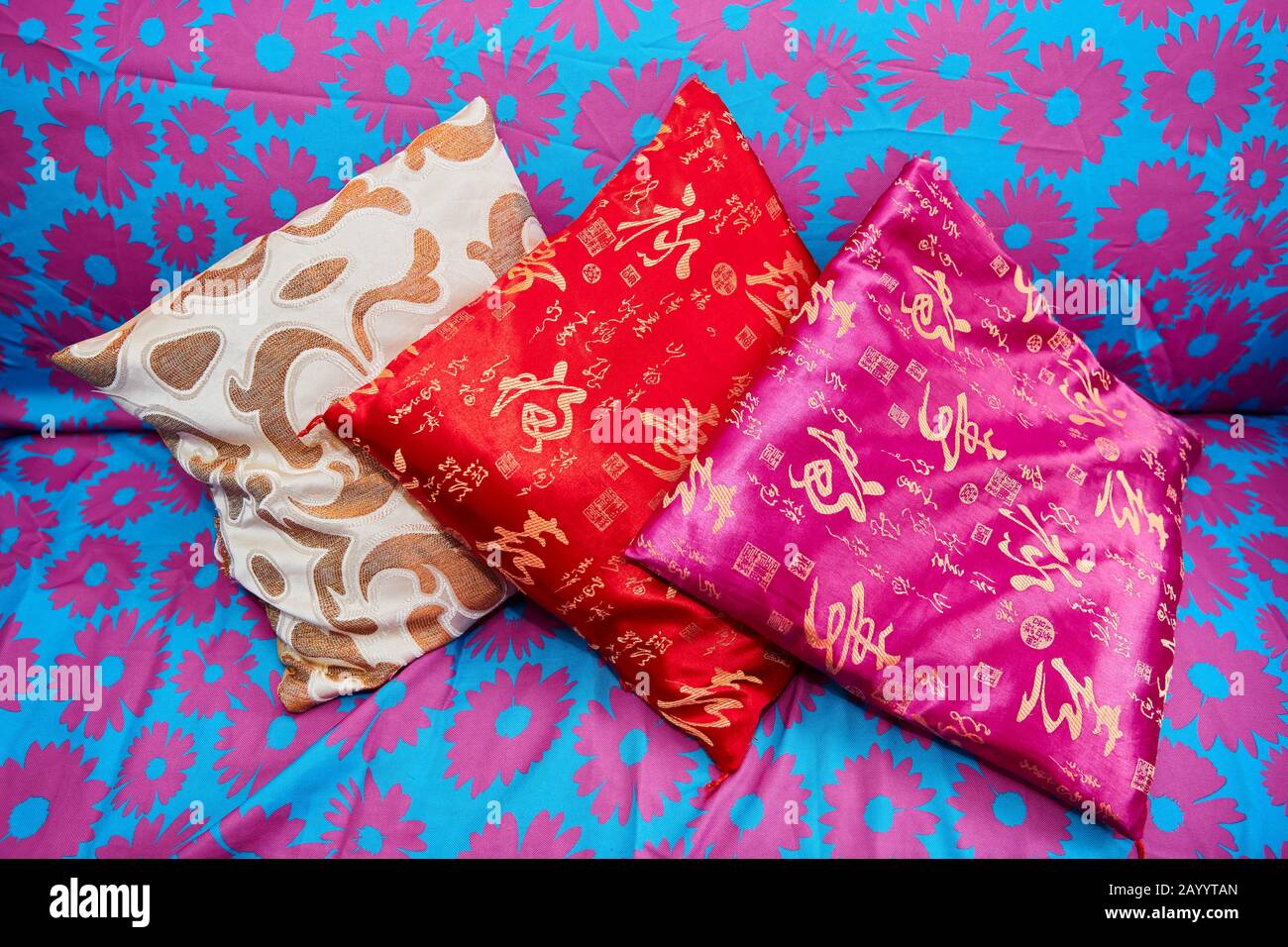 Drei kleine farbenfrohe asiatische Kissen, die auf einem blau gefärbten Sofa mit rosafarbenen Blumenmustern aufliegen Stockfoto