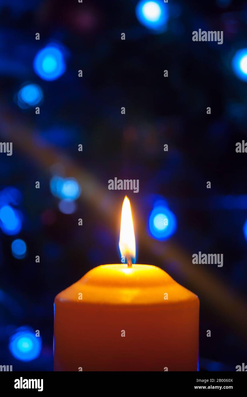 Eine große Kerze brennt vor dem Hintergrund einer Girlande mit strahlendem Licht. Vertikales Foto, Unschärfe. Mystische esoterische Romantik Divination Stimmung getauft Weihnachts-Karol-Setcer Stockfoto