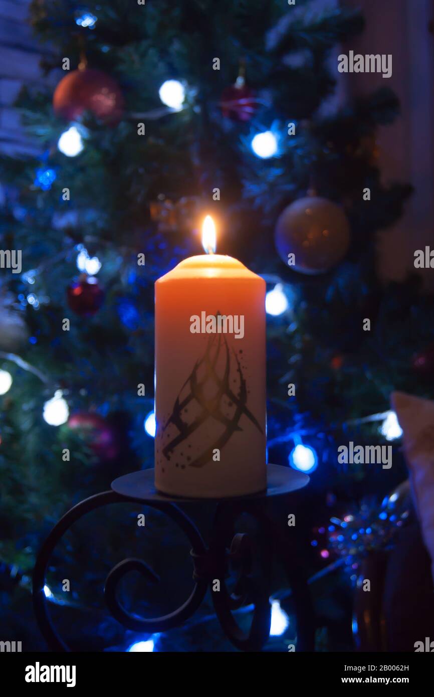 Eine große Kerze brennt vor dem Hintergrund einer Girlande mit strahlendem Licht. Vertikales Foto, Unschärfe. Mystische esoterische Romantik Divination Stimmung getauft Weihnachts-Karol-Setcer Stockfoto