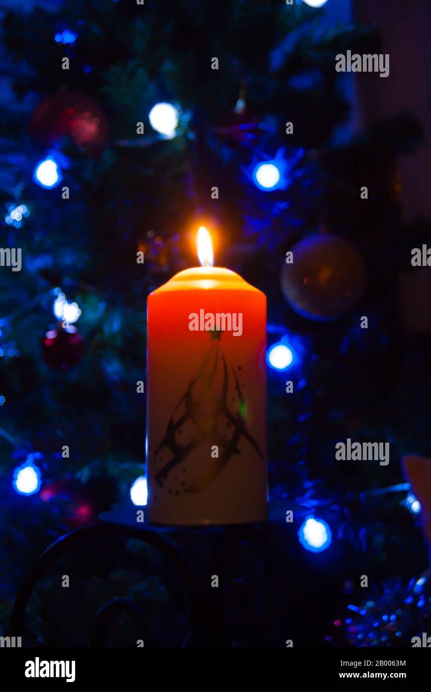 Eine große Kerze brennt vor dem Hintergrund einer Girlande mit strahlendem Licht. Vertikales Foto, Unschärfe. Mystische esoterische Romantik Divination Stimmung getauft Weihnachts-Karol-Setcer Stockfoto