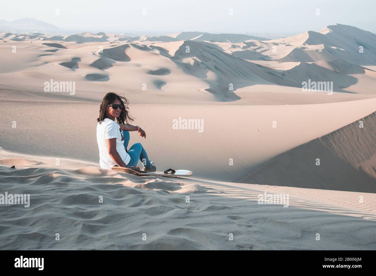 Frau, die Sandboarding in den Wüstensanddünen von Huachina in Peru, Südamerika, genießt Stockfoto