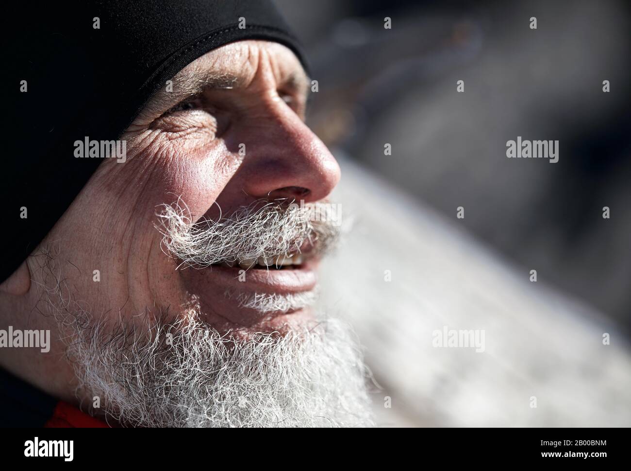 Porträt eines älteren Läufermannes mit grauem Bart, der vor dem Hintergrund der Winterberge lächelt Stockfoto