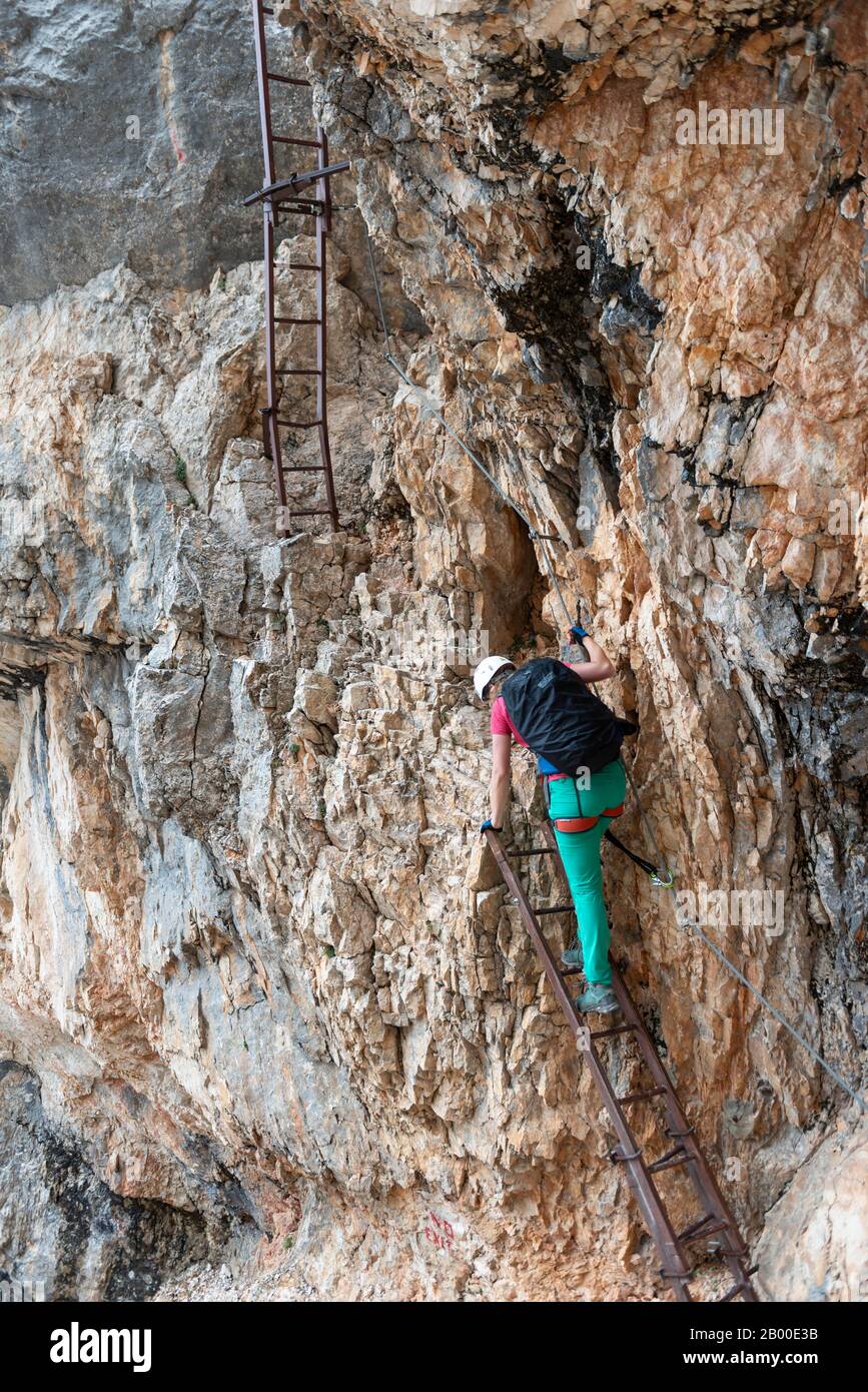 Junge Frau, Wanderer steigt die Leiter hinunter, während sie in einem auf einem Stahlkabel gesicherten Klettersteig Über den Klettersteig Francesco Berti, Sorapiss-Rundkurs, klettert Stockfoto
