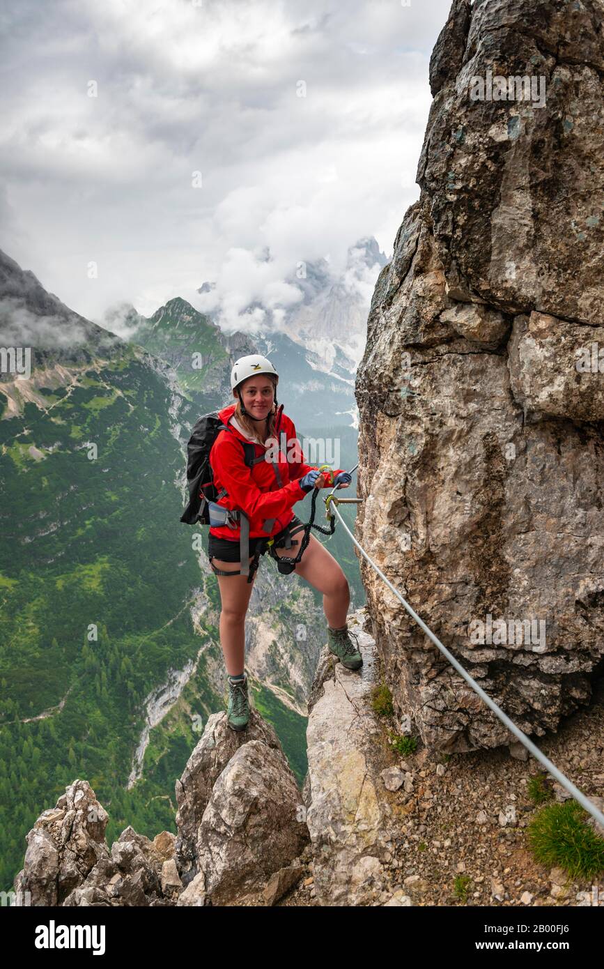 Junge Frau, Wanderer, die in einem Klettersteig Vandelli, Sorapiss-Rundkurs, Berge mit niedrigen Wolken, in den Dolden, Belluno, Italien, eine Felswand erklimmen Stockfoto