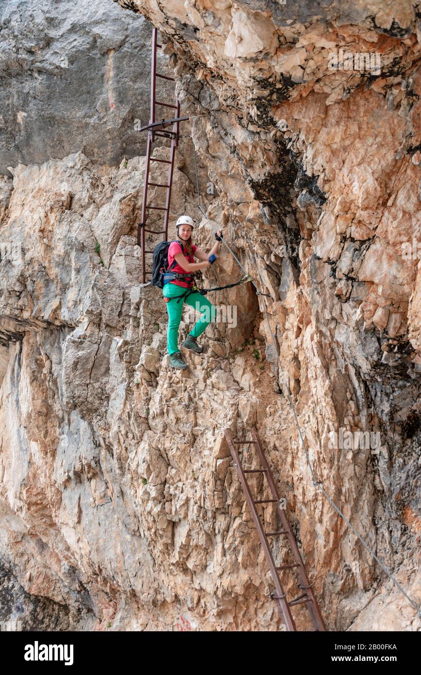 Junge Frau, Wanderer steigt die Leiter hinunter, während sie in einem auf einem Stahlkabel gesicherten Klettersteig Über den Klettersteig Francesco Berti, Sorapiss-Rundkurs, klettert Stockfoto