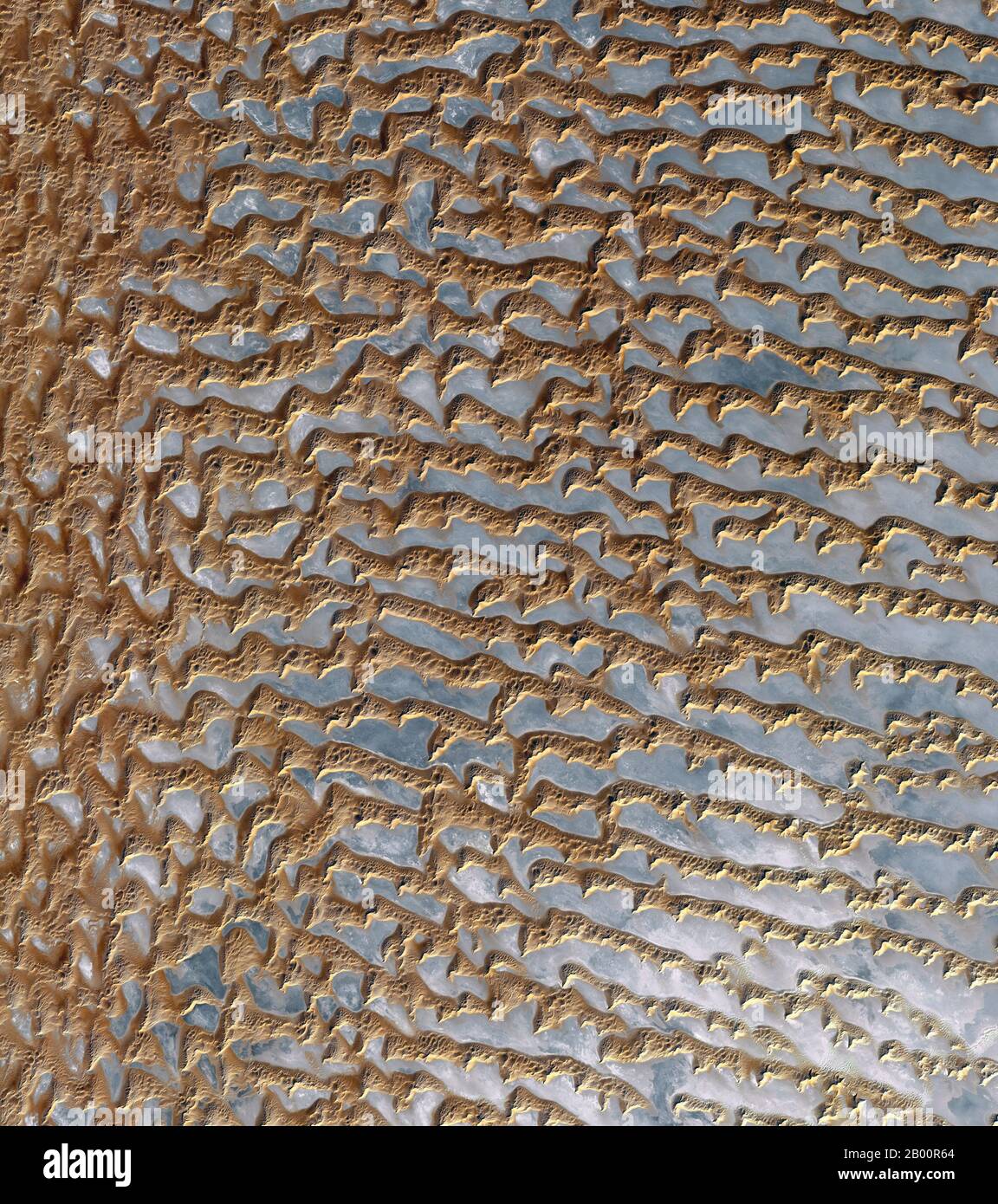 Arabien: Ein Blick aus dem Raum der Sanddünen in Rub' al Khali, ‘das leere Viertel’ auf Arabisch, einer riesigen und trockenen Wüste, die den größten Teil des südlichen Drittels der Arabischen Halbinsel umfasst. Das Bild, das vom Advanced Spaceborne Thermal Emission and Reflection Radiometer (ASTER) an Bord des NASA-Satelliten Terra aufgenommen wurde, zeigt Dünen als braun mit grauen Regionen, die die darunter liegenden Kiesebenen sind. Die Entfernung zwischen parallelen Dünen, die 330 Meter (1,080 Fuß) in der Höhe erreichen können, ist etwa 1.5 bis 2.5 km (0.9 bis 1.6 Meilen). Das Gebiet ist weder bewohnt noch von Menschen durchzogen, obwohl es ein Leben gibt. Stockfoto