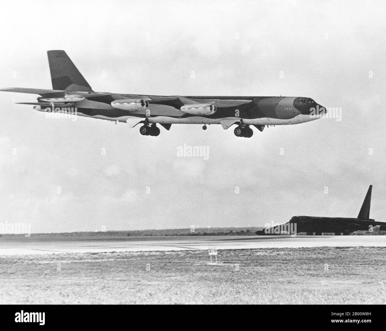 Guam: Eine USAF B-52D Stratofortress wird von einer USAF B-52G überschattet, die von einer Bombenmission über Hanoi 1972 zurückkehrt. Ein B-52D Stratofortress-Flugzeug wartet neben der Start- und Landebahn, während sich eine B-52G während der Operation Linebacker der Landung nähert. Die Flugzeuge sind vom Strategic Air Command. Der zweite Indochina-Krieg, in Amerika als Vietnamkrieg bekannt, war ein militärischer Konflikt aus der Zeit des Kalten Krieges, der in Vietnam, Laos und Kambodscha vom 1. November 1955 bis zum Fall von Saigon am 30. April 1975 stattfand. Stockfoto