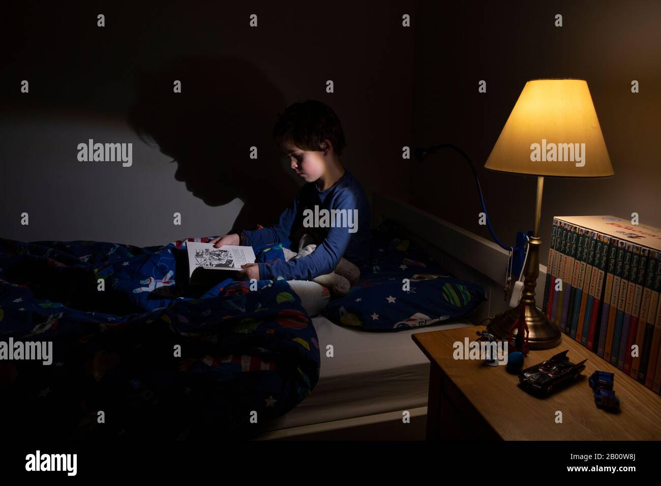 6 Jahre alter Junge, der nachts in seinem Schlafzimmer, England, Großbritannien, ein Enid Blyton Buch liest Stockfoto