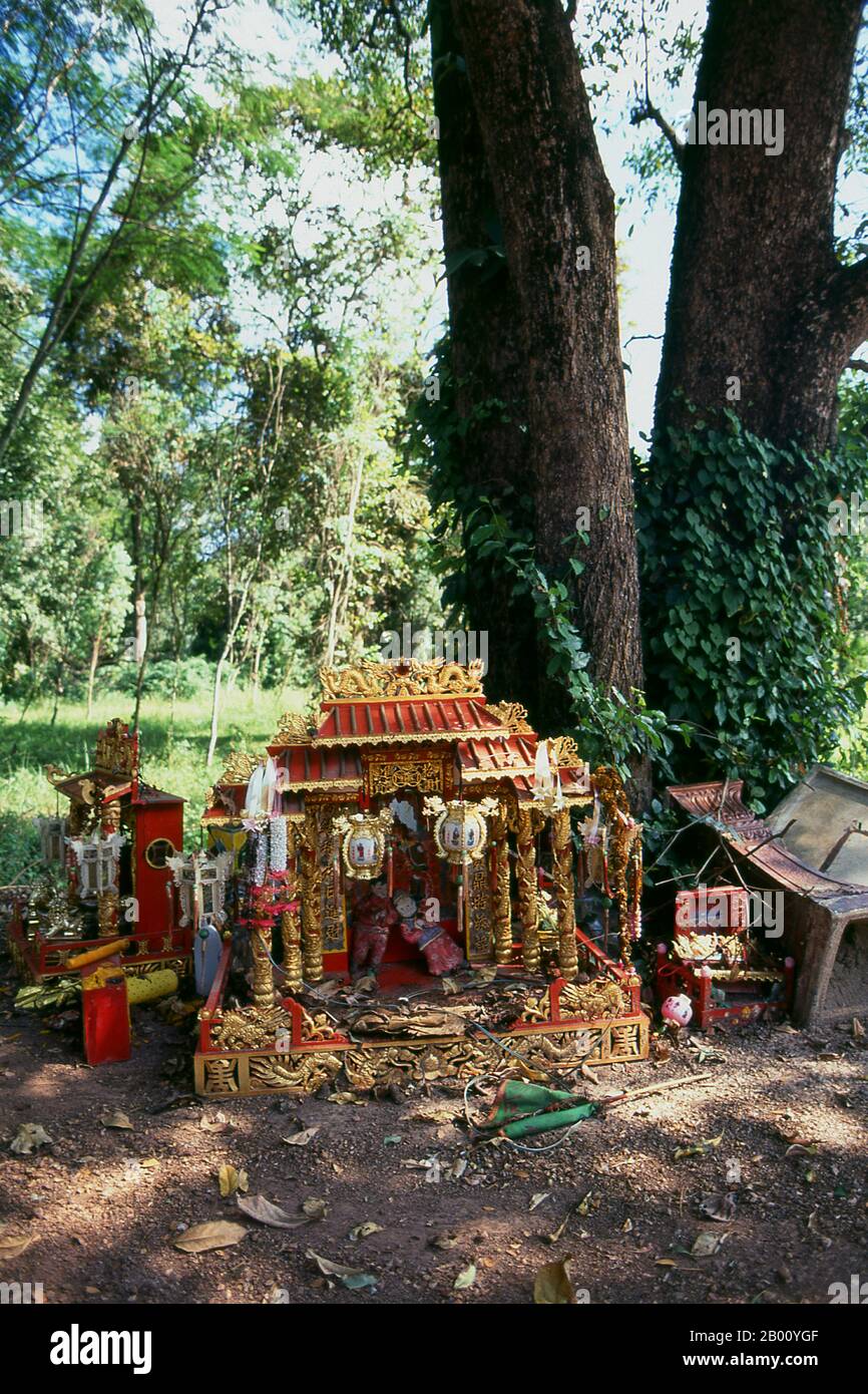 Thailand: Chinesische Geisterhäuser und Ahnen-Schreine um einen Baum in der Nähe des Kamphaeng Phet lak mueang oder Stadtpfosten, Kamphaeng Phet Historical Park. Ein Geisthaus ist ein Schrein zum Schutzgeist eines Ortes. Sie sind in der Regel in den südostasiatischen Ländern Burma, Kambodscha, Laos und Thailand zu finden. Die meisten Häuser und Geschäfte haben ein Geisterhaus, das an einem glückverheißenden Ort, meistens in einer Ecke des Grundstücks, aufgestellt wird. Der Ort kann nach Rücksprache mit einem Brahmanen Priester gewählt werden. Das Geisterhaus ist normalerweise in Form eines Miniaturhauses oder Tempels, der auf einer Säule montiert ist. Stockfoto
