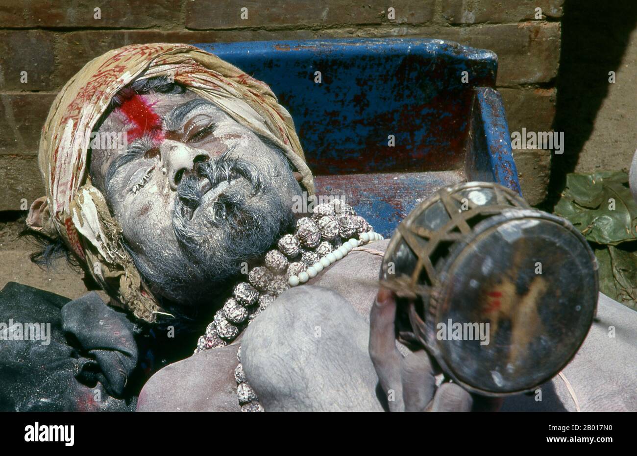 Nepal: Fakir schüttelt sein Tamburin in einer Kathmandu-Straße. Sie sind, verschiedentlich, als Sadhus (Heilige oder 'gute'), Yogis (asketische Praktizierende) bekannt, Fakiren (asketischer Sucher nach der Wahrheit) und Sannyasine (wandernde Bettelmönchen und Asketen). Sie sind die asketischen – und oft exzentrischen – Praktizierenden einer strengen Form des Hinduismus. Geschworen, irdische Wünsche abzuwerfen, entscheiden sich manche dafür, als Anchoriten in der Wildnis zu leben. Andere sind weniger pensioniert, vor allem in den Städten und Tempeln des nepalesischen Kathmandu-Tals. Stockfoto