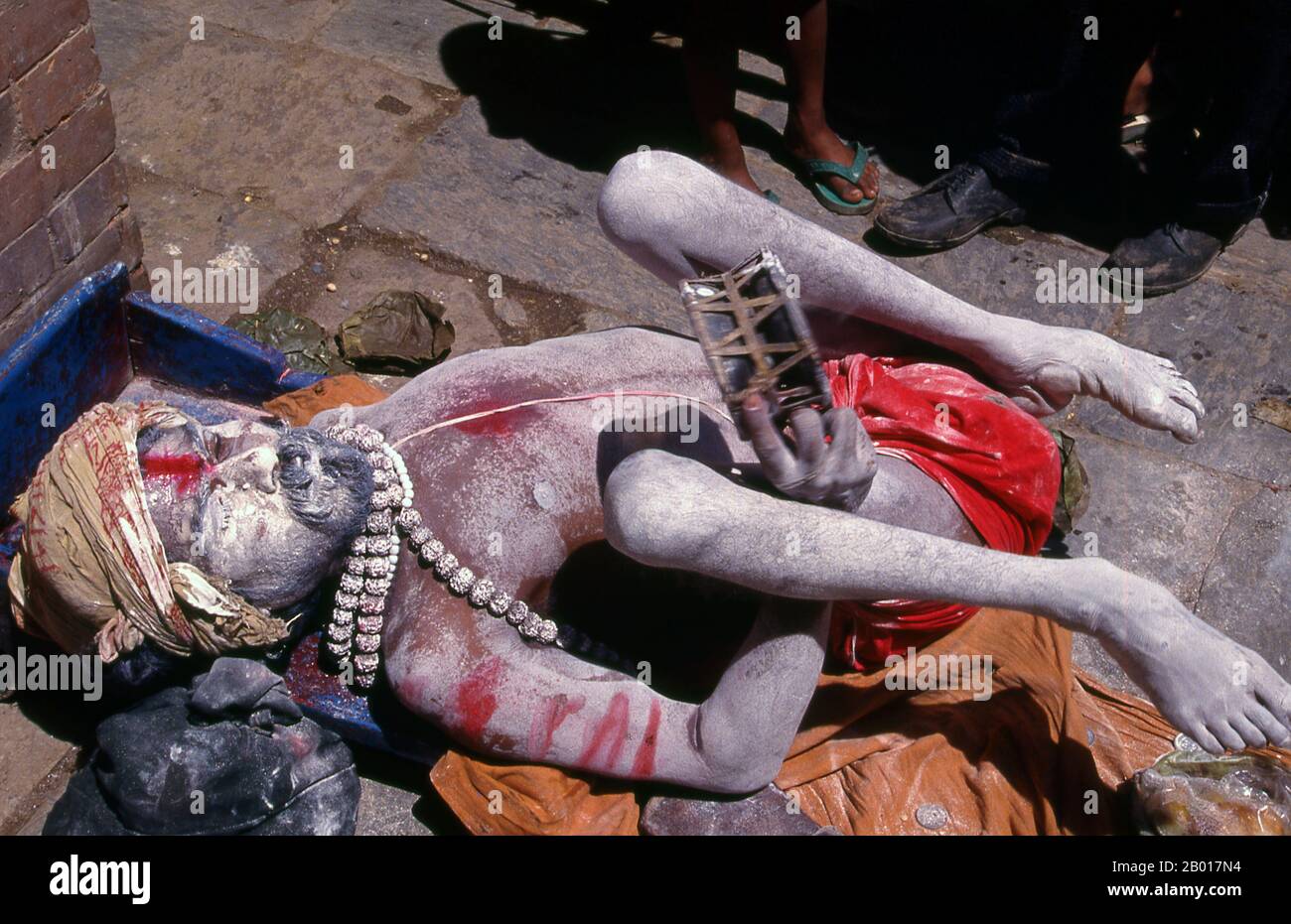 Nepal: Fakir schüttelt sein Tamburin in einer Kathmandu-Straße. Sie sind, verschiedentlich, als Sadhus (Heilige oder 'gute'), Yogis (asketische Praktizierende) bekannt, Fakiren (asketischer Sucher nach der Wahrheit) und Sannyasine (wandernde Bettelmönchen und Asketen). Sie sind die asketischen – und oft exzentrischen – Praktizierenden einer strengen Form des Hinduismus. Geschworen, irdische Wünsche abzuwerfen, entscheiden sich manche dafür, als Anchoriten in der Wildnis zu leben. Andere sind weniger pensioniert, vor allem in den Städten und Tempeln des nepalesischen Kathmandu-Tals. Stockfoto