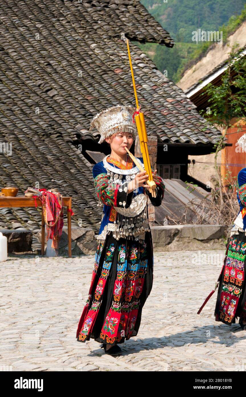 China: Miao-Frau spielt ein traditonales Instrument im Dorf Langde Shang, südöstlich von Kaili, Provinz Guizhou. Der Lusheng (auch lu sheng geschrieben; in der Hmong-Sprache Qeej und ausgeprägte Gaeng) ist ein chinesisches Musikinstrument mit mehreren Bambuspfeifen, die jeweils mit einem freien Rohr ausgestattet sind, das in einem langen Blasrohr aus Hartholz montiert ist. Es hat meistens fünf oder sechs Pfeifen mit unterschiedlichen Tonhöhen und ist somit ein polyphones Instrument. Es ist in Größen von sehr klein bis zu mehreren Metern Länge erhältlich. Stockfoto