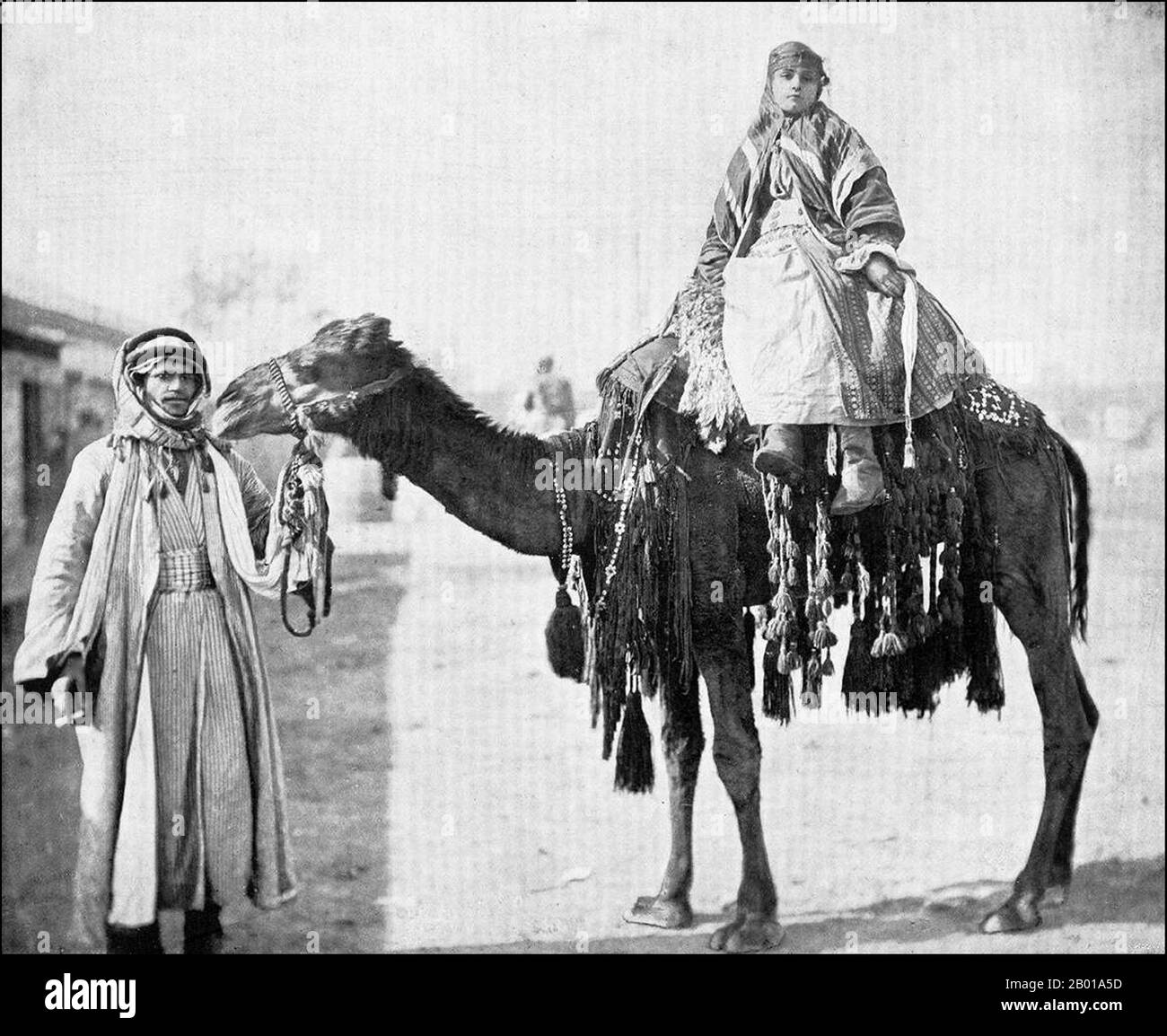 Syrien: Beduinenfrau auf einem Kamel geführt von ihrem Mann, c. 1905. Die Beduinen (aus dem arabischen badawi, pl. badawiyyūn) gehören zu der überwiegend wüstenbewohnten arabischen Volksgruppe. Konkret bezieht sich der Begriff nur auf die "Kamelzüchtiger" Stämme, aber aufgrund wirtschaftlicher Veränderungen sind viele mittlerweile angesiedelt oder züchten Schafe. Auch aufgrund sprachlicher und kultureller Veränderungen wird der Begriff heute häufig auf vielfältige Weise entweder für Araber im Allgemeinen oder für Wüstenbewohner oder Nomaden verwendet. In Syrien leben die Beduinen überwiegend in der Wüste östlich und südlich des Landes. Stockfoto Syrien: Beduinenfrau auf einem Kamel geführt von ihrem Mann, c. 1905. Die Beduinen (aus dem arabischen badawi, pl. badawiyyūn) gehören zu der überwiegend wüstenbewohnten arabischen Volksgruppe. Konkret bezieht sich der Begriff nur auf die "Kamelzüchtiger" Stämme, aber aufgrund wirtschaftlicher Veränderungen sind viele mittlerweile angesiedelt oder züchten Schafe. Auch aufgrund sprachlicher und kultureller Veränderungen wird der Begriff heute häufig auf vielfältige Weise entweder für Araber im Allgemeinen oder für Wüstenbewohner oder Nomaden verwendet. In Syrien leben die Beduinen überwiegend in der Wüste östlich und südlich des Landes. Stockfoto