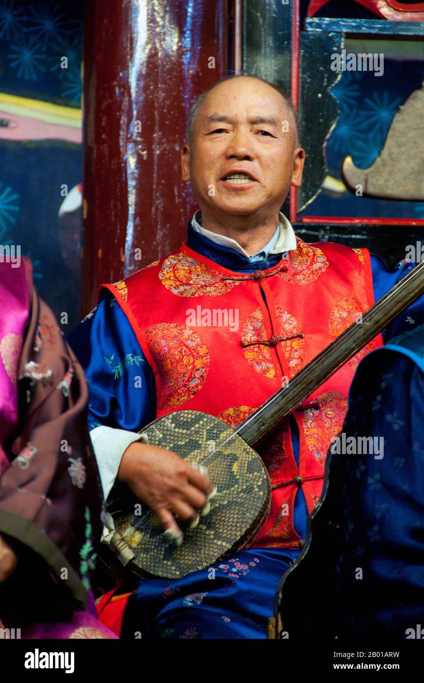China: Ein Mann spielt einen Sanxian, das Naxi (Nakhi) Folk Orchestra, die Naxi-Orchesterhalle, Lijiang Old Town, Provinz Yunnan. Naxi-Musik ist 500 Jahre alt und hat mit ihrer Mischung aus literarischen Texten, poetischen Themen und musikalischen Stilen der Tang-, Song- und Yuan-Dynastien sowie einigen tibetischen Einflüssen einen eigenen, einzigartigen Stil und Züge entwickelt. Es gibt drei Hauptstile: Baisha, Dongjing und Huangjing, alle mit traditionellen chinesischen Instrumenten. Die Naxi oder Nakhi sind eine ethnische Gruppe, die am Fuße des Himalaya im Nordwesten der Provinz Yunnan lebt. Stockfoto